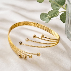 May include: A gold-toned cuff bracelet featuring five parallel, textured wire bands that converge at one end and terminate in small, polished spherical beads at the other open end, creating a layered, multi-strand appearance with a metallic finish.
