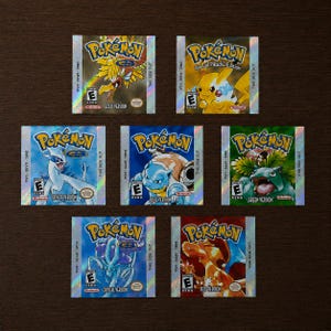 Op de afbeelding: Zeven rechthoekige Nintendo Game Boy videospelcartridges met Pokémon-illustraties. De labels bevatten de versies Gold, Special Pikachu Edition, Silver, Blue, Green, Crystal en Red, elk met het Pokémon-logo en de ESRB E-beoordeling.