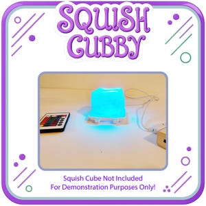 May include: A white square LED light base emitting a bright blue glow, accompanied by a multi-colored remote control and a white power cord. The text SQUISH CUBBY is displayed at the top, with a note stating Squish Cube Not Included.