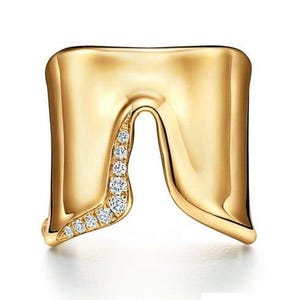 May include: A gold ring with a smooth, polished finish and an open, U-shaped design. One side of the opening features a curved row of small, clear, round-cut stones embedded along the edge, adding a subtle sparkle to the metallic surface.