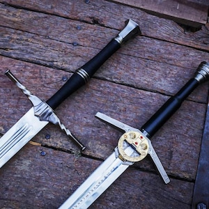 May include: Two metal swords with black handles and silver pommels. The left sword features a twisted crossguard and a central fuller. The right sword displays a circular gold-toned crossguard with engraved details and etched runes on the blade.
