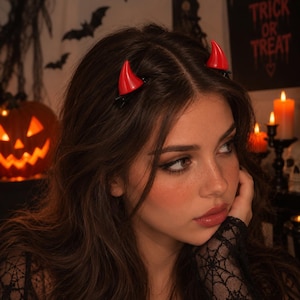 Peut inclure: Une paire de petites cornes de diable rouges et brillantes fixées sur des cheveux châtain foncé. Les cornes sont incurvées et pointues, avec une finition lisse et lustrée. Chaque corne est fixée aux cheveux par une pince noire, placée symétriquement.