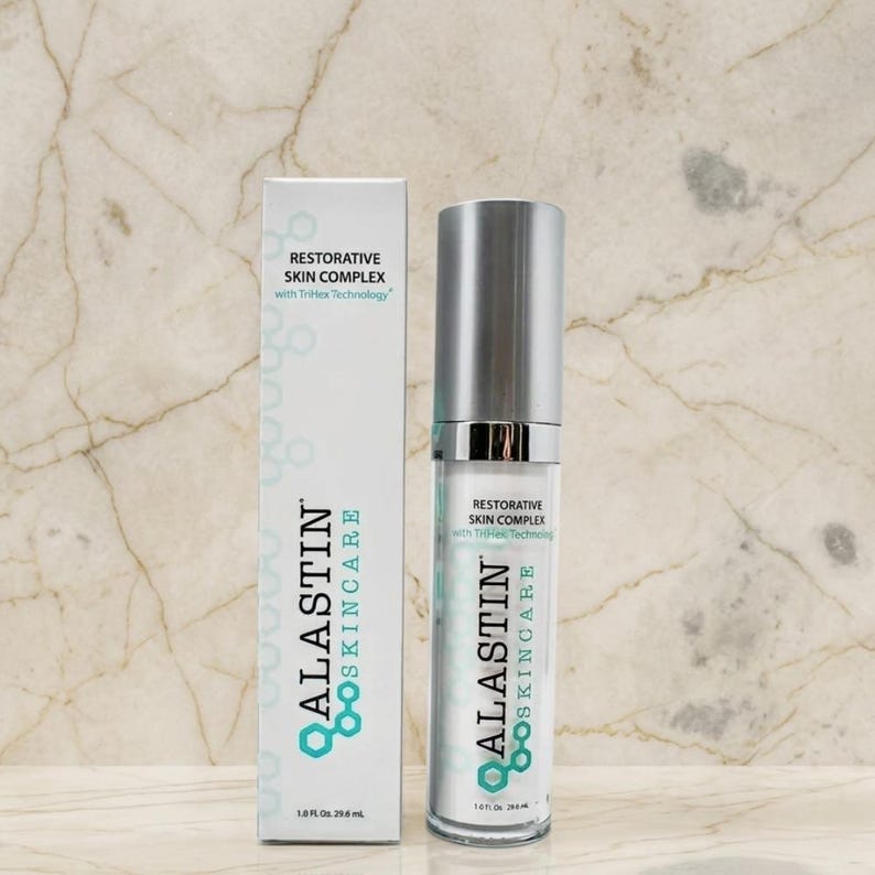 Pu&ograve; includere: Una scatola rettangolare bianca e un flacone cilindrico con erogatore a pompa di Alastin Skincare Restorative Skin Complex con TriHex Technology. Entrambi gli articoli presentano testo nero e verde acqua, con un volume di 29,6 ml.