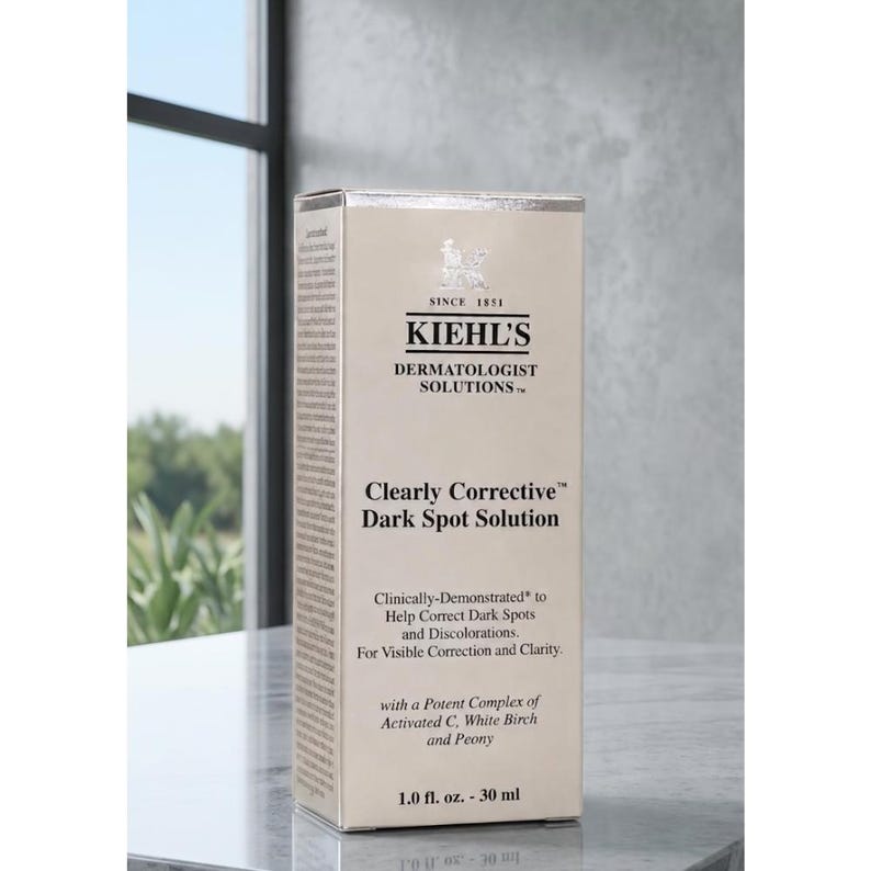 Op de afbeelding: Een rechthoekige Kiehl's Clearly Corrective Dark Spot Solution doos in een lichtbeige kleur met zwarte tekst. De voorzijde toont de merknaam, producttitel en ingredi&euml;nten waaronder Activated C, White Birch en Peony, met 30 ml.
