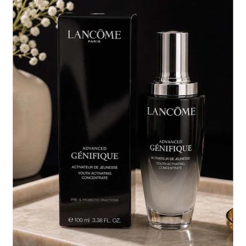 May include: A black Lanc&ocirc;me Advanced G&eacute;nifique Youth Activating Concentrate bottle and its matching rectangular box. The bottle features a silver cap and a black-to-clear gradient glass body. The text reads Lanc&ocirc;me Paris, Advanced G&eacute;nifique, Activateur de Jeunesse, Youth Activating Concentrate, and Pre- & Probiotic Fractions, with 100 ml 3.38 fl. oz. printed on the box.