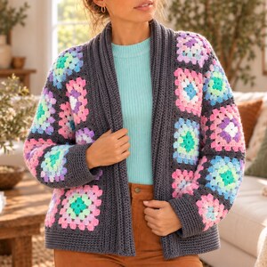 Puede incluir: Un cárdigan de ganchillo gris carbón con un patrón de cuadrados de la abuela en tonos pastel rosa, morado, azul y verde. La prenda tiene cuello y puños acanalados, mangas largas y un diseño frontal abierto con un borde gris oscuro sólido.