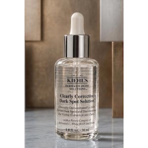 Op de afbeelding: Een doorzichtige glazen fles van Kiehl's Clearly Corrective Dark Spot Solution met een zilveren druppeldop en witte knijper. Het etiket bevat zwarte tekst waaronder 'Since 1851', 'Dermatologist Solutions' en '1.0 fl. oz. - 30 ml' op de voorzijde.