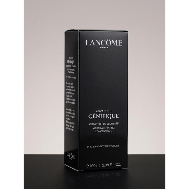May include: A black rectangular skincare product box labeled Lanc&ocirc;me Paris Advanced G&eacute;nifique Youth Activating Concentrate. The front displays white text including Pre- & Probiotic Fractions and the volume 100 ml 3.38 FL. OZ. in a vertical orientation.