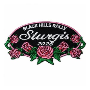 May include: An oval-shaped embroidered patch with a black background, featuring the white text "BLACK HILLS RALLY" and "Sturgis 2026". The design is framed by a pink border and decorated with pink roses and green leaves along the bottom and sides.