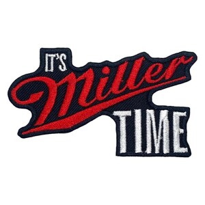 Pode incluir: Um emblema bordado com o texto IT'S em branco, seguido pela palavra miller em letra cursiva vermelha com um sublinhado vermelho, e a palavra TIME em letras maiúsculas brancas, sobre um fundo azul-marinho escuro com borda recortada.