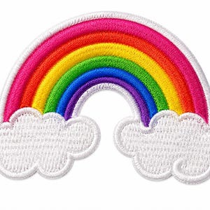 Peut inclure: Un écusson brodé représentant un arc-en-ciel aux bandes concentriques rouge, orange, jaune, verte, bleue et violette. L'arc-en-ciel surplombe deux bases blanches en forme de nuages duveteux de chaque côté, le tout bordé d'un contour blanc.