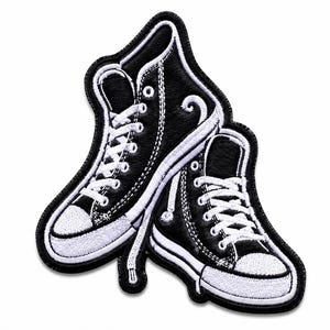 Puede incluir: Un parche bordado que muestra dos zapatillas de deporte de caña alta en blanco y negro. Las zapatillas tienen cordones blancos, punteras de goma blanca y suelas blancas, con partes superiores de tela negra. El parche tiene un borde negro.