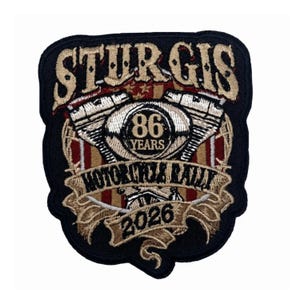 May include: A black embroidered patch featuring the text STURGIS at the top, 86 YEARS in the center, MOTORCYCLE RALLY on a banner, and 2026 at the bottom. The design includes a stylized engine graphic and a red, white, and tan striped background.