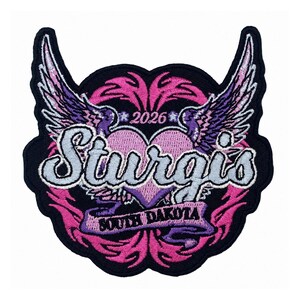 May include: An embroidered patch featuring a central light purple heart flanked by purple and white wings. The text Sturgis is written in large script across the center, with 2026 above and South Dakota on a banner below, all set against a black background.
