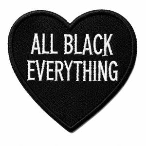 May include: A heart-shaped embroidered patch with a black background and white stitched text that reads ALL BLACK EVERYTHING. The patch features a thick black border and a textured fabric surface, designed for application to clothing or accessories.