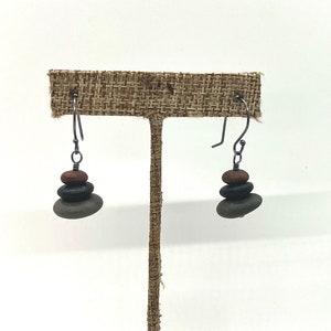 May include: A pair of earrings with a stack of three small stones on each earring. The stones are brown, black, and gray. The earrings are made with silver wire.