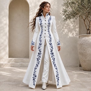 May include: A long-sleeved white coat featuring a high collar and a front button closure. The coat is adorned with vertical dark blue floral embroidery running down the center front and along the sleeve cuffs. It is worn over matching white trousers.