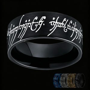 Puede incluir: Un anillo de metal negro cepillado con escritura élfica grabada en blanco alrededor de la banda exterior. El diseño incluye una superficie interior lisa y pulida. Una pequeña fila de cuatro anillos adicionales en azul, plata, oro y negro es visible debajo.