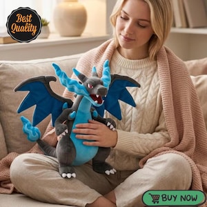 May include: A plush toy of a dark gray and blue dragon-like creature with large wings, a long tail with a blue flame tip, and white claws. The creature has a blue crest on its head, a light blue belly, and an open mouth showing white teeth.