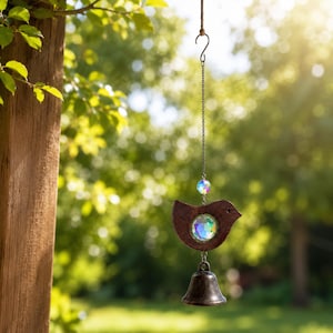 May include: A hanging ornament featuring a dark brown wooden bird silhouette with a circular iridescent crystal center, suspended by a silver-toned chain with an additional iridescent crystal bead and a small dark metal bell at the bottom.