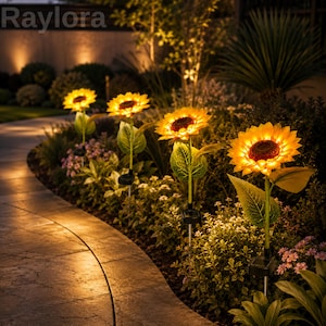 May include: Four solar-powered garden lights shaped like sunflowers with bright yellow petals and dark brown centres. Each flower is mounted on a green stem with leaves and a small square solar panel at the base, illuminating a stone garden path.