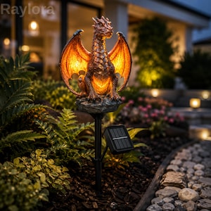May include: A solar-powered garden stake light featuring a sculpted dragon figure with textured bronze-toned scales and wings. The dragon is perched on a rock-like base and emits a warm, glowing orange light from within its body. A small black solar panel is attached to the stake.