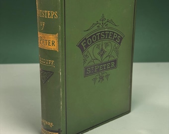 以下が含まれることがあります： 背表紙と表紙に金と黒の文字で「Footsteps of St. Peter」と記された緑色のハードカバー本。表紙にはタイトルが書かれた装飾的なバナーデザインと、複雑な線画のディテールが施されています。