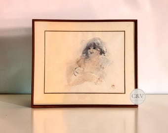 以下が含まれることがあります： 暗い髪の人物の柔らかな印象派の肖像画が描かれた、紙に描かれた水彩画の額装品。このアートワークは、クリーム色のマットボードと小さな赤い署名印が付いた、細いダークブラウンの木製フレームに収められています。