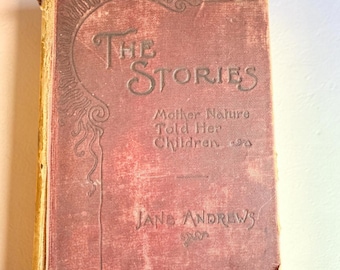 May include: A vintage hardcover book titled The Stories Mother Nature Told Her Children by Jane Andrews. The cover is a faded reddish-brown color with embossed dark lettering and a decorative swirling line design along the left side edge.