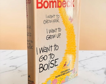以下が含まれることがあります： エルマ・ボンベック著『I Want to Grow Hair, I Want to Grow Up, I Want to Go to Boise』のハードカバー本。表紙には、黄色いレンガの道、蝶、小さな鳥、色とりどりの花がベージュの背景に描かれています。