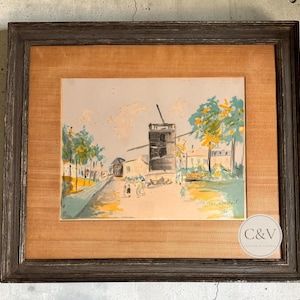 Könnte beinhalten: Ein gerahmtes Gemälde, das eine Windmühle auf einem Dorfplatz mit Bäumen und Figuren in gedeckten Grün-, Gelb- und Brauntönen zeigt. Das Kunstwerk ist mit Maurice Utrillo signiert und befindet sich in einem dunklen, verwitterten Holzrahmen.