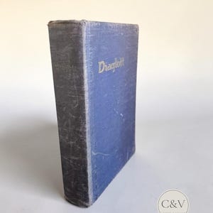 May include: A vintage hardback book with a worn blue fabric cover. The word Diaglott is printed in gold lettering on the front cover. The spine and edges show signs of wear and fading, with a textured surface and a rectangular shape.