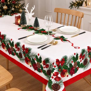 May include: A white rectangular tablecloth featuring a festive Christmas print of green pine branches, red bows, holly leaves, red berries, and brown pinecones along the edges and center, finished with a solid red border trim.