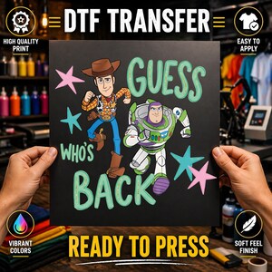 Op de afbeelding: Een zwart DTF-transfervel met Woody en Buzz Lightyear uit Toy Story. De tekst luidt GUESS WHO'S BACK in lichtgroene letters. Het ontwerp bevat roze en blauwgroene sterren verspreid rond de personages op een donkere achtergrond.
