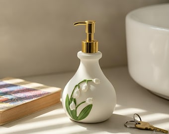 Dispenser di sapone in ceramica con motivo floreale e pompa in acciaio inox. Accessorio da bagno da appoggio nei colori oro e argento.