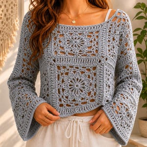 May include: A light blue long-sleeve crochet top featuring a square neckline and intricate floral-inspired granny square patterns throughout the body and sleeves. The garment has a cropped length and wide, flared sleeves with an openwork design.