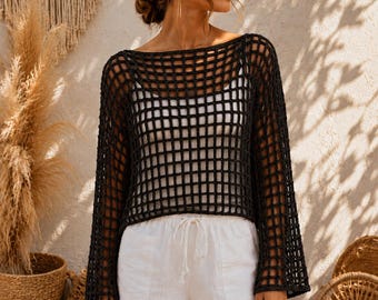 May include: A black long-sleeve crochet jumper featuring a wide grid pattern and a boat neckline, worn over a white camisole, paired with white shorts that have a drawstring waist and cuffed hems, creating a layered outfit ensemble.