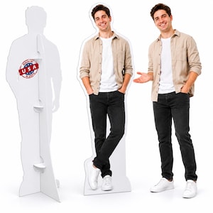 Puede incluir: Una figura de cartón a tamaño real de una persona sonriente con camisa beige sobre una camiseta blanca, vaqueros negros y zapatillas blancas. El soporte trasero incluye un sello circular rojo con la inscripción Made in USA.