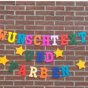 Könnte beinhalten: Ein mehrfarbiges Banner aus einzelnen Buchstaben, die den Text WUNSCHTEXT UND FARBEN bilden. Die Buchstaben sind in verschiedenen leuchtenden Farben wie Orange, Gelb, Blau, Pink, Rot und Grün gehalten und mit hellvioletten und gelben Sternen verziert.