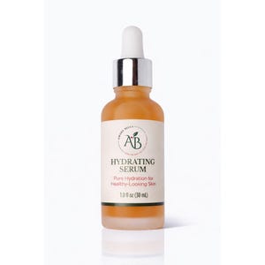 May include: A glass dropper bottle containing an amber-colored hydrating serum. The white label features the text Amare Bella AB, Hydrating Serum, Pure Hydration for Healthy-Looking Skin, and 1.0 fl oz (30 mL) with a silver collar and white dropper top.