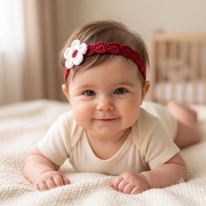 May include: A crochet headband featuring a deep red scalloped band and a white flower accent with a red center. The headband is worn across the forehead, showcasing a detailed yarn texture and a contrasting color scheme of white and dark red.