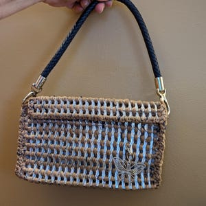 May include: A woven brown and white handbag with a black leather strap and a silver butterfly charm.