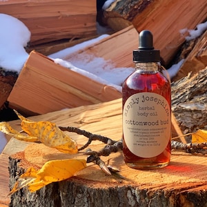 May include: A glass bottle of Simply Josephine herbal body oil with a black dropper top. The bottle is labeled "cottonwood bud" and contains 4 ounces of oil.