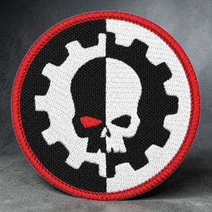 May include: A circular embroidered patch featuring a split black and white gear design. A skull is centered over the gear, also split into black and white halves. The skull has a single red eye on the black side. The patch has a red stitched border.