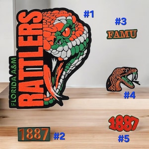 May include: A collection of embroidered patches featuring a large snake head with orange, green, and white scales, the text "FLORIDA A&M RATTLERS", a rectangular "1887" patch, a "FAMU" patch, a smaller snake head patch, and a curved "1887" patch.
