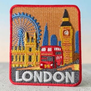 May include: A rectangular embroidered patch featuring a London cityscape with the London Eye, Big Ben, and a red double-decker bus. The design includes a tan background, a red border, and the word LONDON in white capital letters at the bottom.