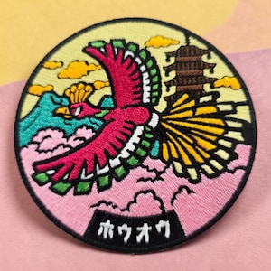 May include: A circular embroidered patch featuring a stylized pink and yellow bird with green-tipped wings flying over pink clouds and a teal mountain. A brown pagoda stands in the background against a pale yellow sky. The Japanese text "ホウオウ" is embroidered in white on a black rectangular base at the bottom.