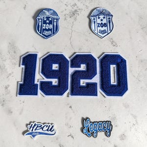 May include: Two blue and white shield-shaped patches with the text ZΦB and 1920, a large blue and white chenille patch displaying the number 1920, and two smaller patches featuring the text HBCU Made and Legacy in blue and white embroidery.