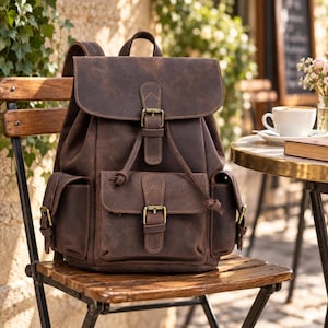 Puede incluir: Una mochila de cuero marrón oscuro que presenta una solapa principal grande con cierre de hebilla, un bolsillo frontal con una hebilla a juego y dos bolsillos laterales. Incluye un asa superior y correas ajustables con herrajes de metal.