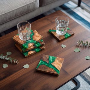 May include: A set of square coasters made from natural wood and vibrant green resin. The coasters feature organic wood grain patterns integrated with smooth, translucent green resin sections. Two clear glass tumblers sit on the coasters.